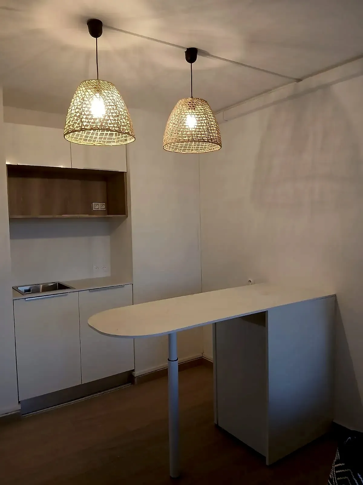 Coin cuisine terminé : caissons blancs, niche effet bois, plan effet marbre blanc, et l'îlot à bout arrondi devant