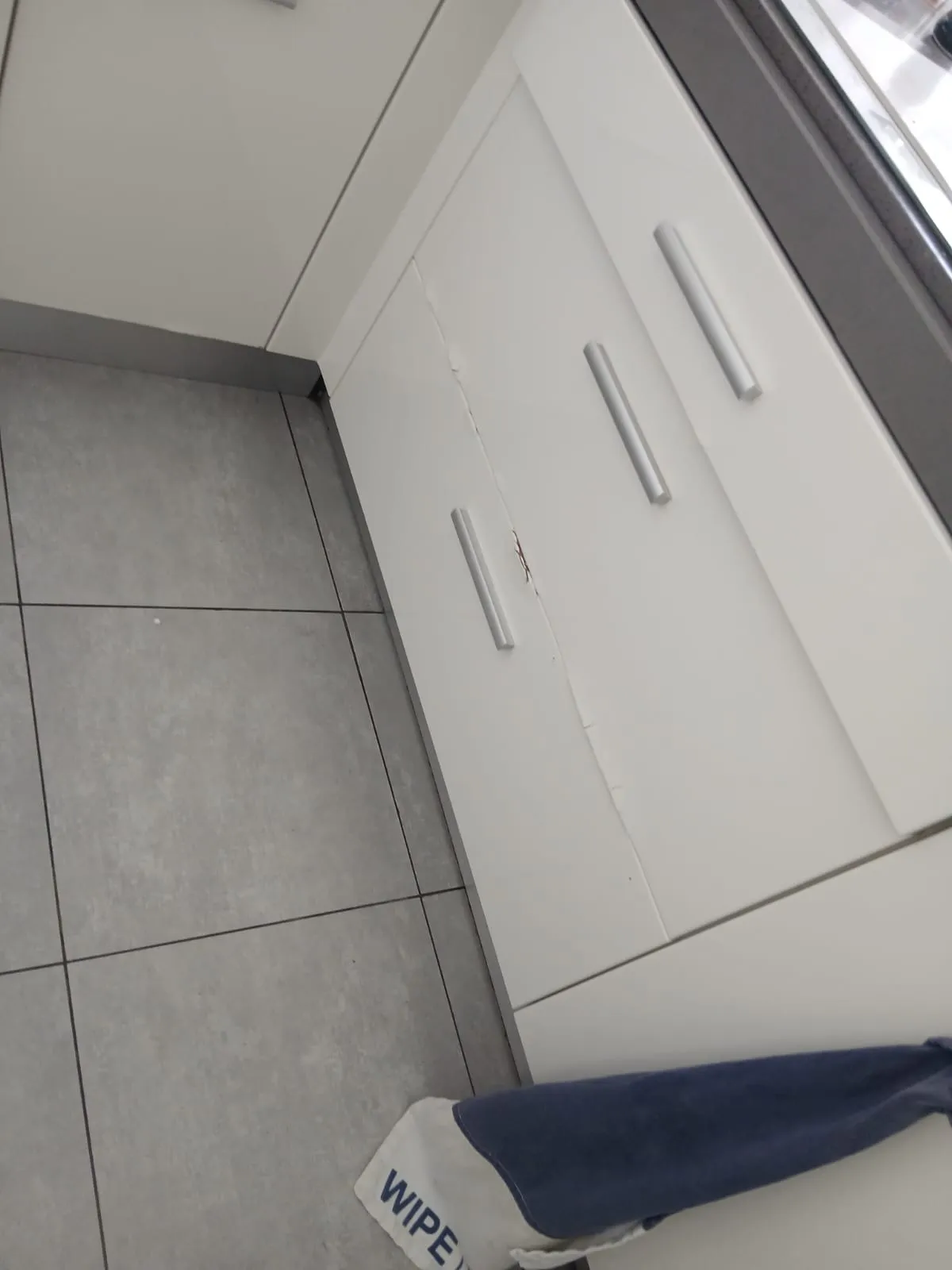 Porte de meuble de cuisine blanche fendue sur toute sa hauteur, le panneau ayant gonflé et décollé